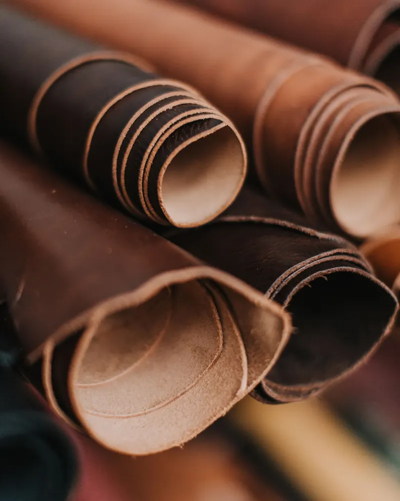 Rolled hides of dark brown and tan leather, showing natural grain and cut edges